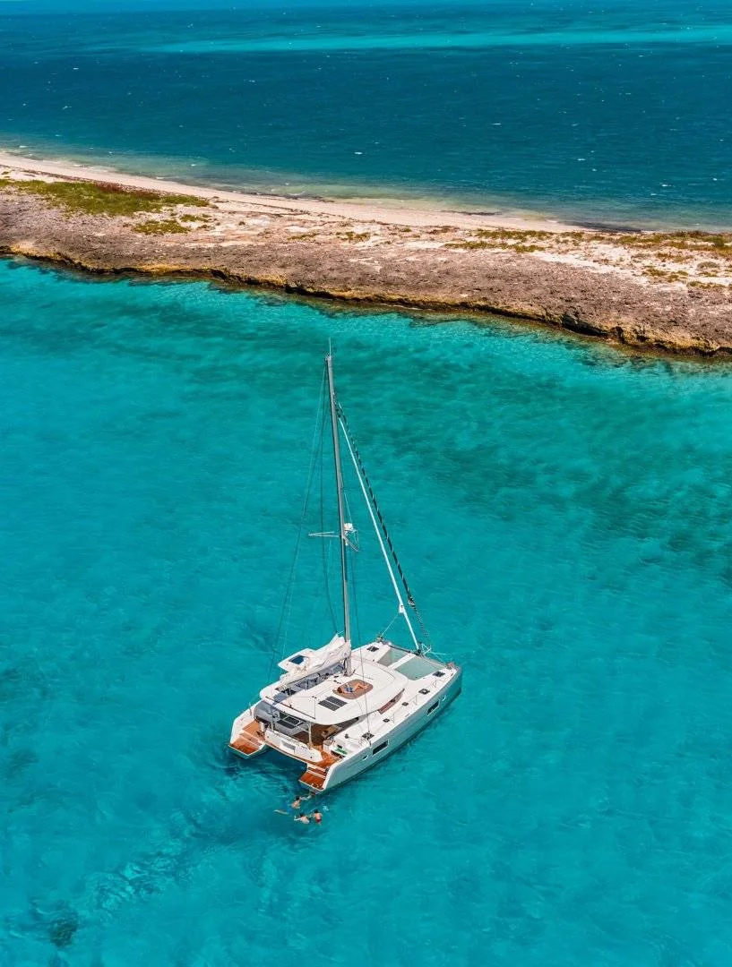 A catamaran anchored in clear turquoise water beside a rocky island