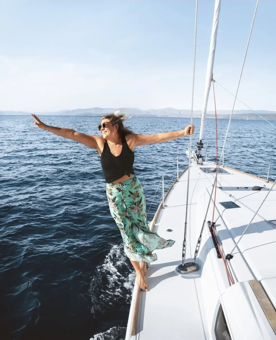 A woman opening her arms to the sea breeze on the bow of a sailing boat